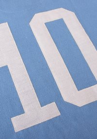 Tela azul claro con grandes números "1" y "0" blancos bordados, presentando un patrón acanalado texturizado. El diseño está centrado en la tela.