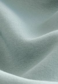 Una tela de color azul claro muestra una textura suave y lisa con un delicado patrón de punto, dispuesta de manera que resalte su forma flexible.