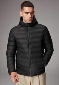 Sort isoleret pufferjakke med lynlås fortil, vandret quiltning, hætte og elastiske manchetter. Glat tekstur og minimalistisk design.