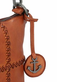 Sac en cuir marron avec des coutures élaborées, doté d'un pendentif en métal en forme d'ancre attaché par une sangle en cuir. Fermeture éclair en haut.