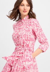 Vestito camicia rosa con stampa paesaggistica dettagliata, colletto con bottoni, cintura in vita e maniche a tre quarti. Realizzato in tessuto leggero.
