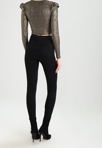 Schwarze enge Jeans kombiniert mit einem metallischen, glitzernden Cropped-Top mit langen Ärmeln und Rüschendetails an den Schultern.
