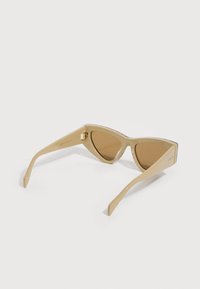 Gafas de sol beige con forma de ojo de gato y lentes marrones, vista lateral angular que muestra el logo de Gucci en la patilla.
