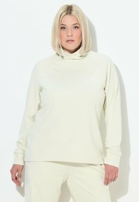 Helles beiges Langarmshirt mit hohem Kragen, gerippter Textur und Berglogo-Detail auf der linken Brust, kombiniert mit passenden Hosen.