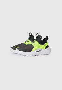 Des chaussures noires et jaunes fluo à enfiler, avec un dessus texturé, une semelle blanche tachetée et un branding Nike bien en évidence à l'avant et sur le côté.