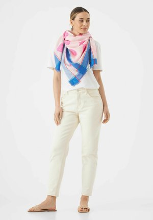 Sciarpa a righe rosa e blu con bordi frangiati, indossata su una camicia bianca, abbinata a pantaloni color crema e sandali intrecciati beige.