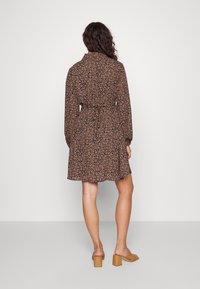 Svart blommig klänning med långa ärmar och snäv midja. Tyget har små rosa och vita blommor, med en svängig nederkant. Bruna klacksandaler.