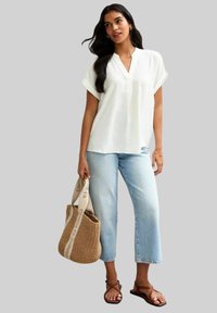 Vit kortärmad blus med V-ringning, tillsammans med ljusblå cropped jeans. En vävd väska med logoband fulländar looken. Bruna sandaler.
