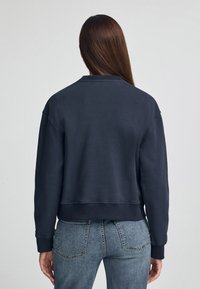 Sudadera de marina con mangas largas, diseño recortado y puños de canalé. Tejido suave con textura lisa, con cuello redondo y costuras mínimas.