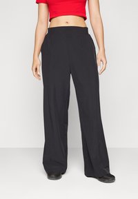 Pantaloni larghi in tessuto nero, con cintura elastica e tasche laterali. Texture liscia con una vestibilità morbida.