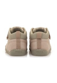 Zapatos mid-top de ante marrón con acentos beige, presentan una suela plana, forma redonda y una correa ajustable de Velcro. El logo está en el talón.