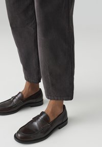 Dark brown leather loafers with decorative stitching, paired with charcoal corduroy pants featuring a straight cut and cuffed hem.