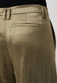 Oliegroene broeken van gestructureerde stof, met een slank ontwerp, riemlussen en een enkele achterzak met een gestroomlijnde vorm.