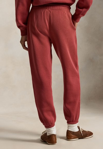 Røde joggebukser med elastisk midjebånd og ribbestrikkede mansjetter, med sidelommer. Brukt sammen med brune sko og hvite sokker.