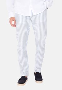 Pantaloni a righe blu chiaro e bianchi realizzati in un tessuto leggero con vestibilità slim, abbinati a espadrillas blu scuro.