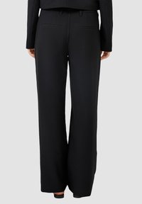Pantalons larges noirs avec une texture lisse, ceinture avec passants, et deux poches arrière. Design simple, sans fermetures ni motifs visibles.