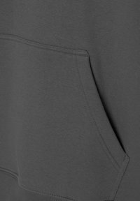 Gros plan sur la poche kangourou d'un sweat-shirt gris foncé avec des coutures visibles et la texture du tissu.