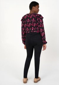 Un jean skinny noir assorti à un blouse à manches volantes arborant un motif floral dans des nuances de rose et de blanc. Texture lisse, design ajusté.