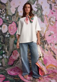 Hvid oversized top med korte ærmer, kombineret med lyseblå bukser med brede ben. Modellen bærer et tørklæde med blomsterprint og har en farverig taske.