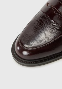 Brauner Lederloafer mit glänzender Oberfläche, der eine genähte Naht um die Sohle und ein breites Riemen-Detail über dem Spann aufweist.