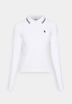 Valkoinen pitkähihainen polo-paita, jossa on ribbikuviointi, puolen vetoketjun kaulus ja tummansinisiä rannetta koristavat yksityiskohdat kauluksessa. Paidassa on myös pieni logo.