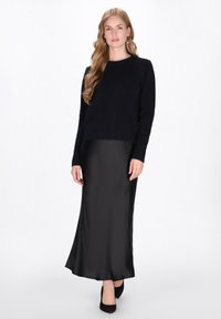 Marineblauwe gebreide trui, ronde hals, lange mouwen, gecombineerd met een zwarte satijnen maxi rok. Zwarte hoge hakken maken de outfit compleet.