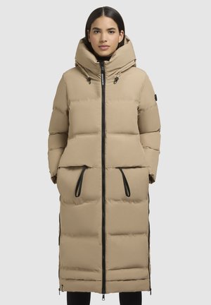 Beige pufferjack met een lange structuur, capuchon, twee voorzakken en zwarte ritsen. Kenmerkt zich door een gewatteerde textuur en verstelbare trekkoorden.