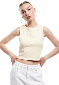 Korte mouwloze top in zacht geel, met een ronde hals. Gladde textuur met een getailleerd silhouet, gecombineerd met witte, high-waisted broek.