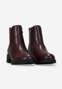 Bottines bourgogne en cuir brillant avec un talon carré et une fermeture éclair sur le côté. Présente une texture lisse et un design minimaliste.