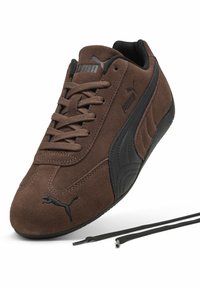 Bruine suède sneaker met zwarte accenten, voorzien van een getextureerd zijpaneel, een ronde neus en zwarte veters. Het Puma-logo is duidelijk zichtbaar.