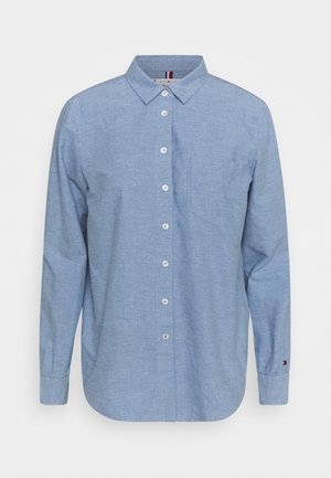 Chemise bleu clair à manches longues boutonnée, avec une poche poitrine et un col classique, présentée sur fond blanc.