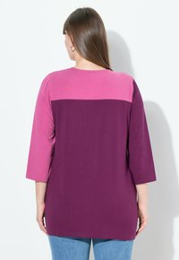 Langarmshirt met een roze en paarse colorblock ontwerp. Zachte stof, afgeronde zoom, relaxte pasvorm. Achteraanzicht toont een gladde textuur en simpele styling.