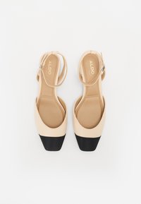 Chaussures à talons ouverts beige avec un embout carré noir. Fabriquées en matériau lisse, elles présentent une fine bride de cheville avec une boucle.