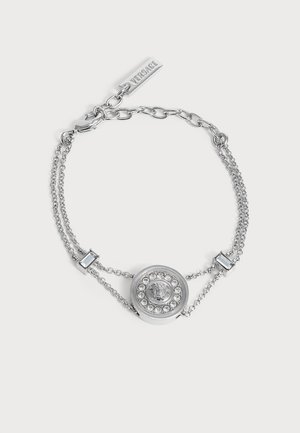 Pulsera de doble cadena plateada con medallón redondo en el centro adornado con cristales y una cara grabada, con una etiqueta con el logo de Versace.