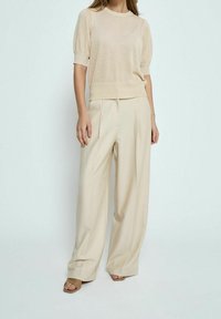 Maglia beige a maniche corte con scollo rotondo, abbinata a pantaloni beige fluidi con pieghe. Tessuto liscio e vestibilità comoda.