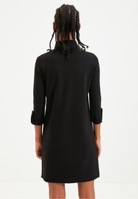 Robe noire droite avec des manches trois-quarts, dotée d'un col et de poignets retroussés. Tissu lisse, design à longueur genou et style minimaliste.