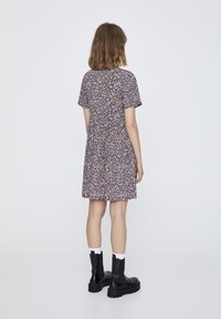 Robe fleurie à manches courtes, motif coloré sur fond sombre, forme évasée. Portée avec des bottines noires épaisses et des chaussettes blanches.