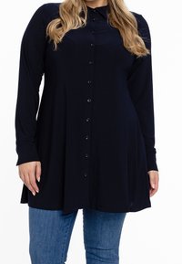 Blusa a maniche lunghe blu navy con colletto, realizzata in un tessuto liscio, caratterizzata da una vestibilità rilassata e orlo inferiore arrotondato.