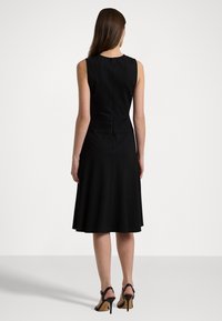 Svart ärmlös klänning med en figursydd överdel och utsvängd kjol, med dragkedja bak, tillsammans med svarta högklackade skor.