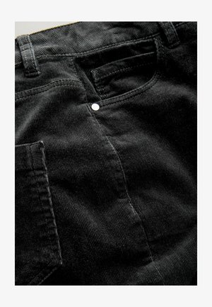 Zwarte corduroy stof met verticale strepen, voorzien van een achterzak en een zilveren knoopdetails nabij de tailleband.