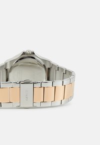 Metallarmbanduhr mit einem Silber- und Roségoldarmband, das polierte Glieder und ein Gehäuse aus rostfreiem Stahl aufweist. Runde Gehäuse mit einem klaren Rückenteil.