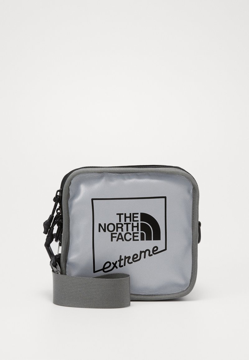 Borsa a tracolla grigia in nylon con chiusura a zip, dotata di un logo nero sulla parte anteriore e di una tracolla grigia regolabile.