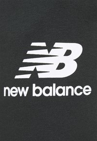 Černá látka s výrazným bílým logem "N" s rychlostními čarami nad ním a textem "new balance" pod ním v čistém, moderním písmu.