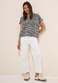 Haut à manches courtes noir et blanc à rayures avec un décolleté en V, associé à un pantalon large blanc et des baskets beiges avec des accents rouges.