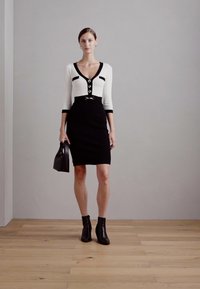 Robe ajustée noir et blanc avec des manches trois-quarts, des détails de boutons et des accents argentés. Portée avec des bottines noires et un petit sac à main.