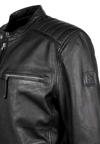 Chaqueta de cuero negra con un bolsillo en el pecho con cremallera, detalles acanalados en los hombros y un parche con logo en la manga. Textura suave.