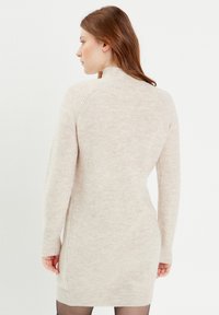 Vestido de punto en suave beis con textura acanalada, mangas largas y cuello alto. Silueta ajustada que llega hasta la mitad del muslo.