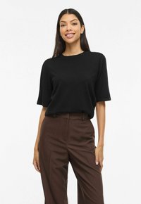 Mustast kergest kangast valmistatud lõdva lõikega lühikeste varrukatega t-särk, mis on kokku sobitatud kõrge vöökohaga pruuni krobelise tekstuuriga pükstega. Pehme tekstuur, lihtne disain.