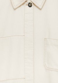 Chemise en coton écru avec fermeture à boutons, col pointu et deux poches poitrine. Présente des détails de couture contrastants beige.