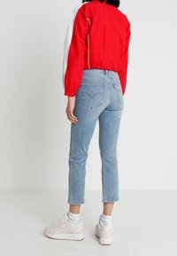 Czerwona i biała kurtka o krótkim kroju, jasnoniebieskie dżinsy o prostym kroju oraz białe trampki, widziane od tyłu.